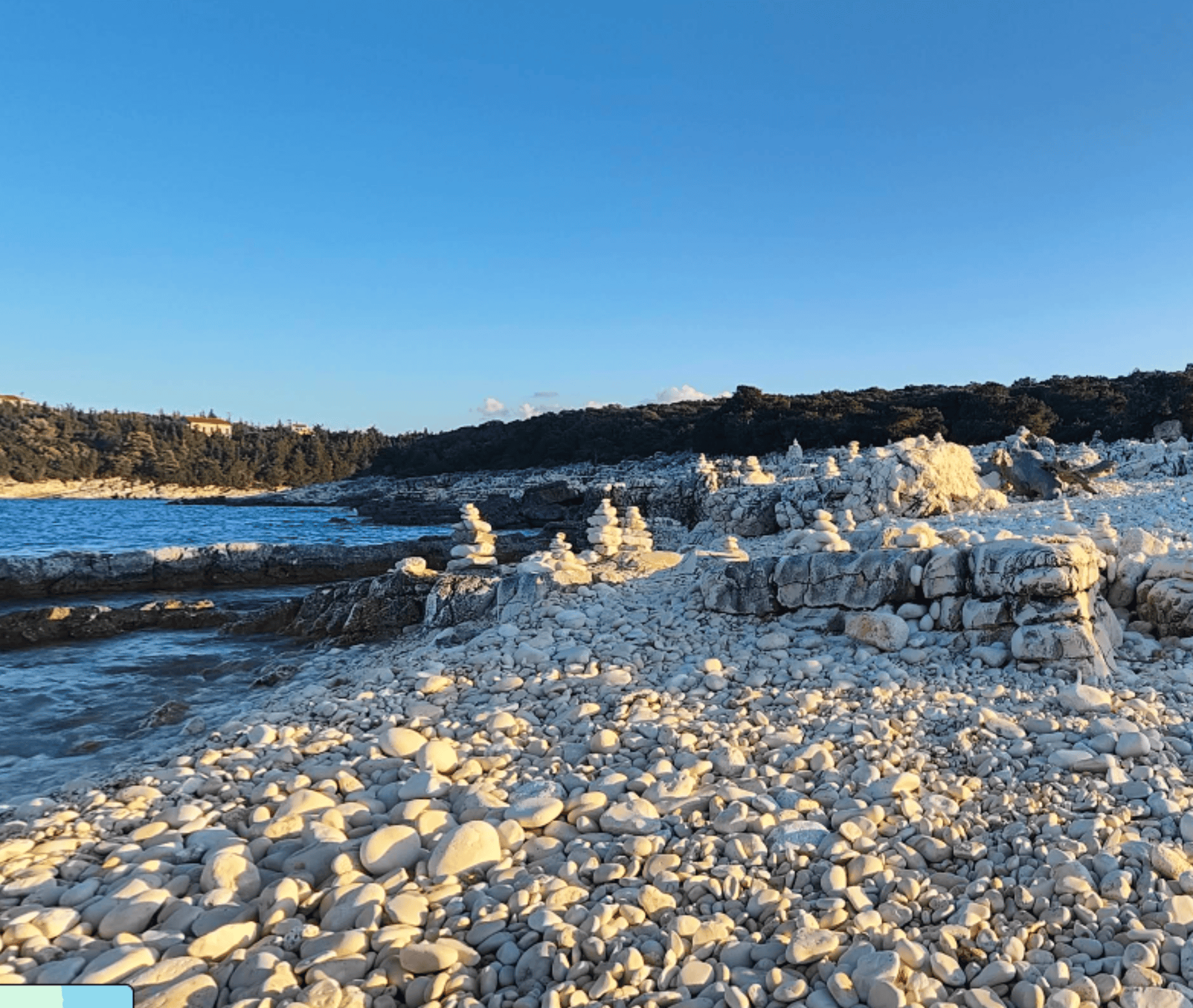 Salt flats at Emplisi Beach with rocky shoreline and clear blue sky.