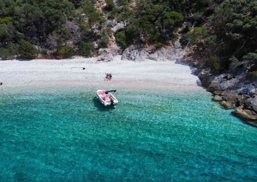 Boat anchored near a scenic beach with clear turquoise waters and lush green surroundings.